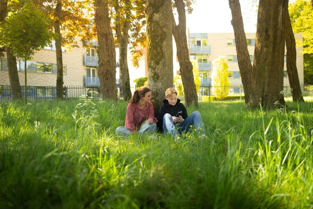Twee jongeren in het gras, samen op een telefoon kijkend
